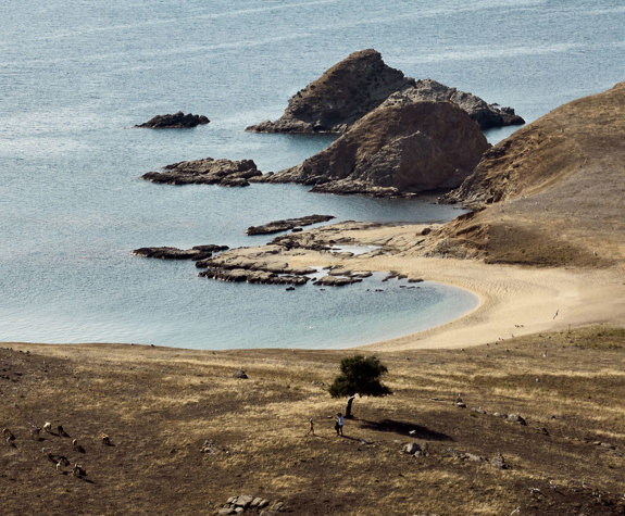 Secluded cove with rocky islets and a sweeping sandy beach, seen from a hillside at Drenia island