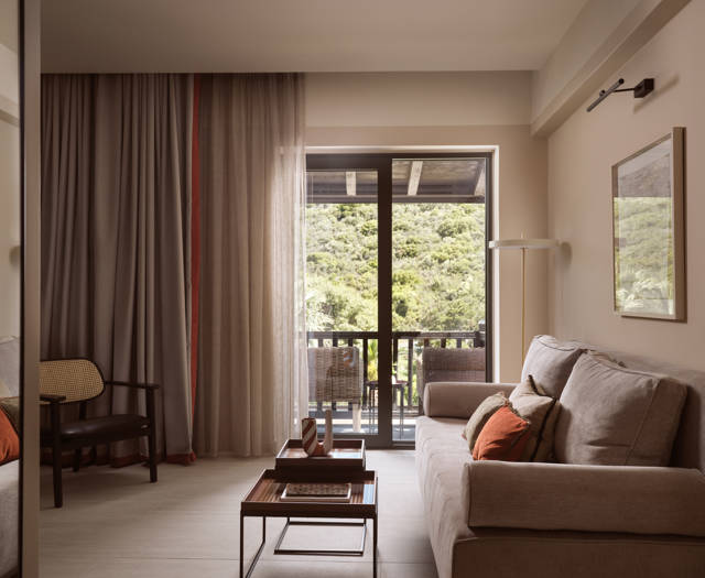 Deluxe suite living area at Eagles Palace with sofa seating, sheer curtains and balcony overlooking the garden