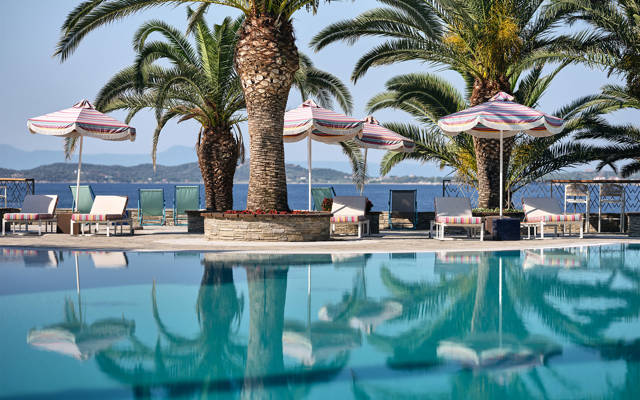 Palm lined pool with striped umbrellas and sea view on a sunny day at Eagles Resort