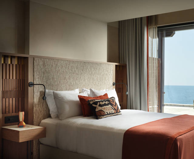 Executive junior suite with king bed, terracotta throw and balcony doors opening to a sea view at Eagles Palace