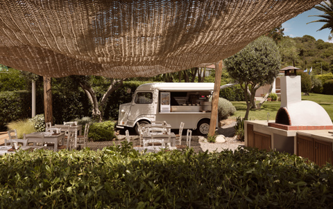 Outdoor dining area with shaded seating, vintage food truck and pizza oven at cantina in Eagles Resort