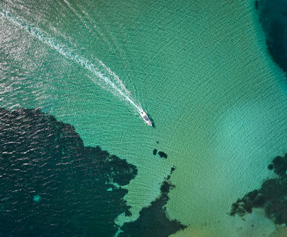 Aerial view of a motorboat cruising over vibrant shallow waters