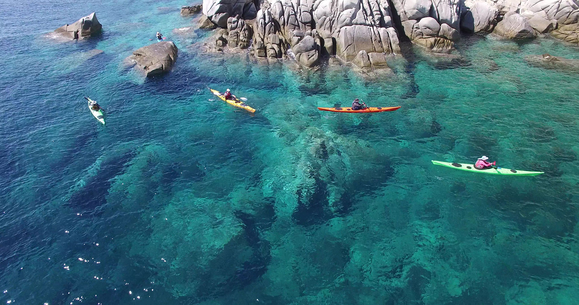 Four brightly colored kayaks paddling through clear waters near rocky coastline at Eagles Resort