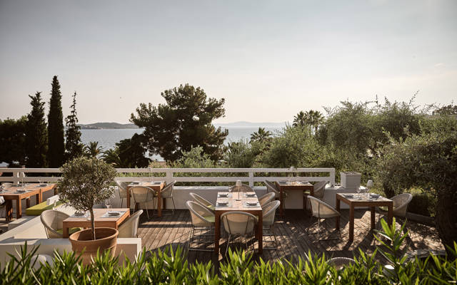 Eleonas restaurant's outdoor terrace with dining tables surrounded by greenery overlooking the sea at Eagles Resort