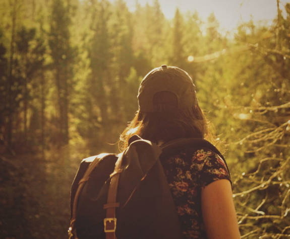 Woman hiking through a forest trail during golden hour, wearing a backpack an cap at Eagles Resort