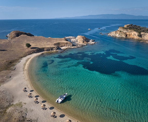 Aerial view of Drenia island sandy beach with sun loungers and umbrellas and a sailing boat in the sea