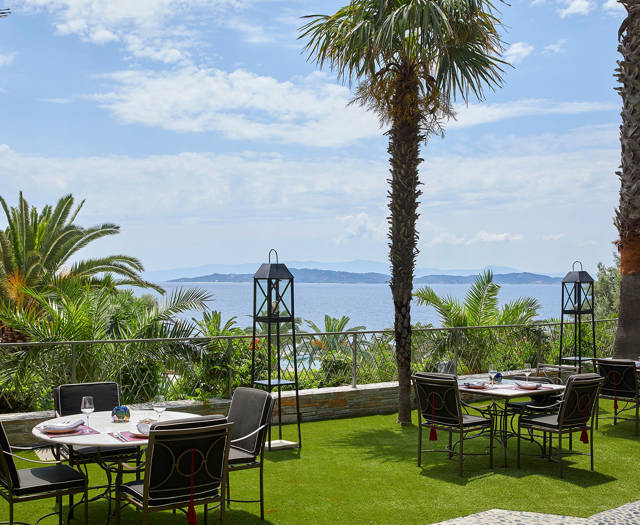 Outdoor dining tables on green terrace with palm trees and sea view at Vinum restaurant in Eagles Resort