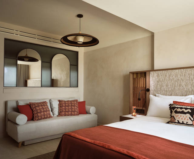 Executive junior suite with bed and terracotta bedding, sofa with cushions and arched mirror at Eagles Palace